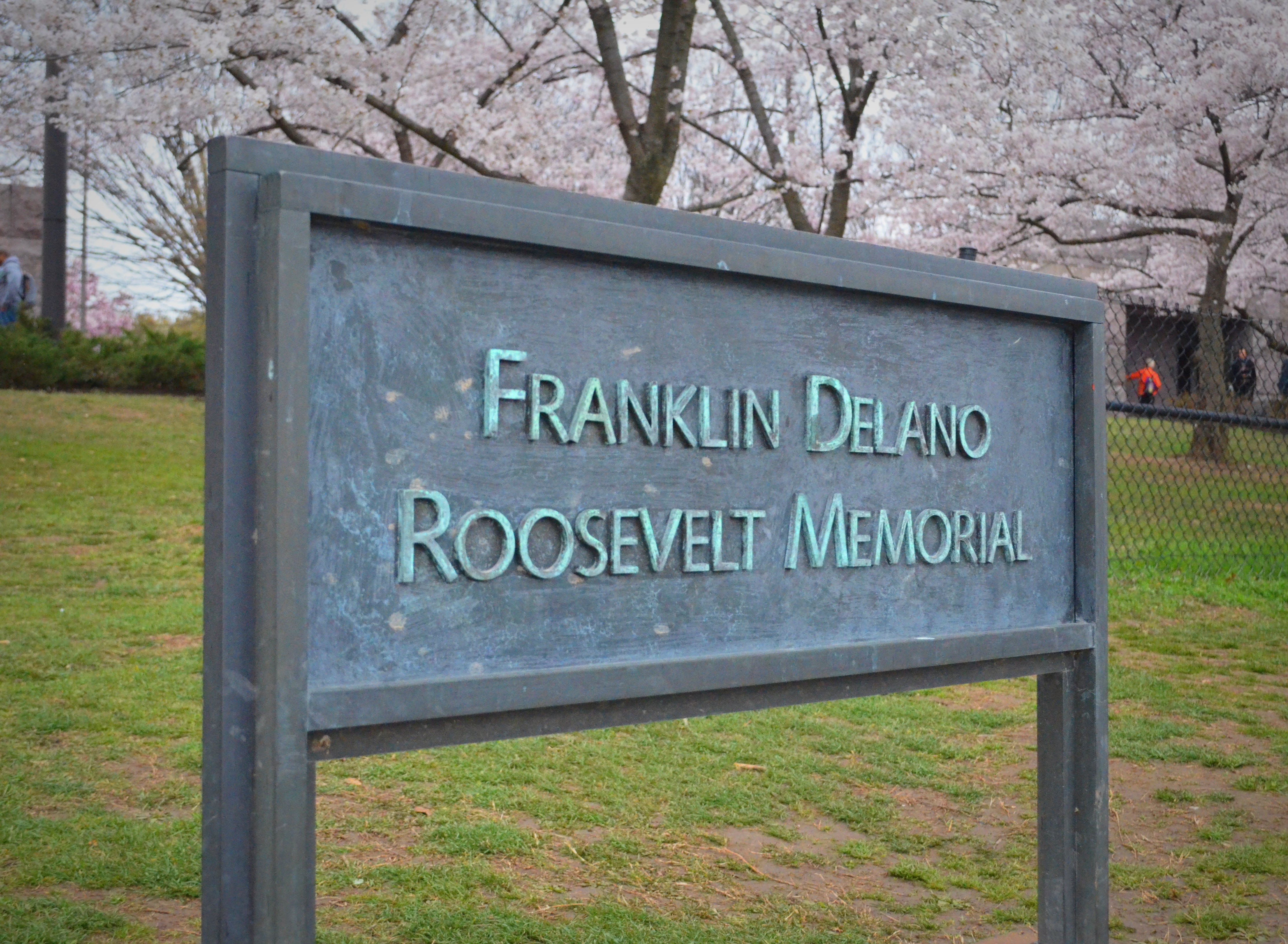 Blue sign with franklin delano roosevelt memorial written on it with cherry blossoms behind it, FDR, franklin delano roosevelt, FDR memorial, franklin delano roosevelt memorial, fdr memorial dc, fdr memorial washington dc, franklin delano roosevelt washington dc, franklin delano roosevelt washington dc, washington dc, dc, dc monuments, dc memorials, dc photography, dc travel, dc history, dc travel blog, dc traveling blog, dc travel photography, dc travels, traveling in dc, traveling in washington dc,
